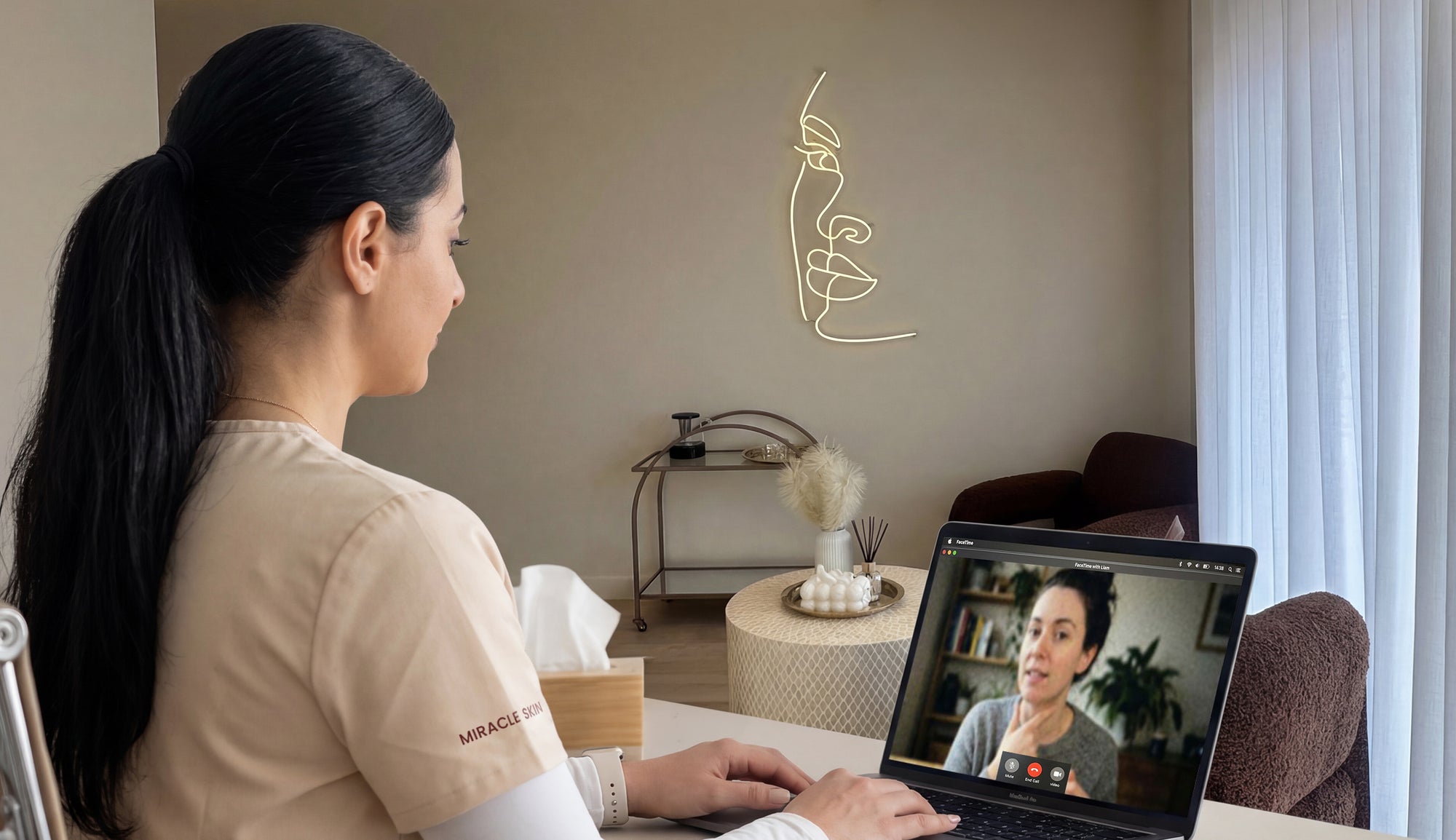 Woman in a beige shirt using a laptop in a clinic virtual consultation setting
