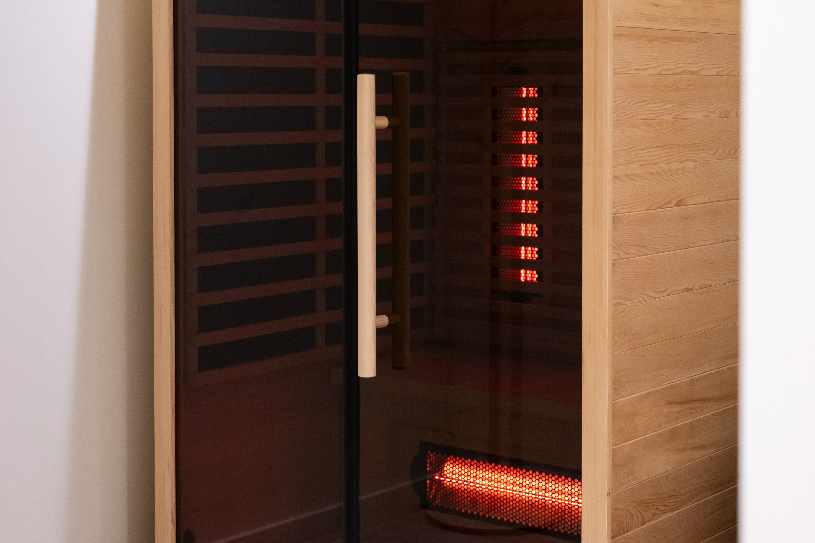 Infrared sauna with wooden exterior and glass door showing interior lights.